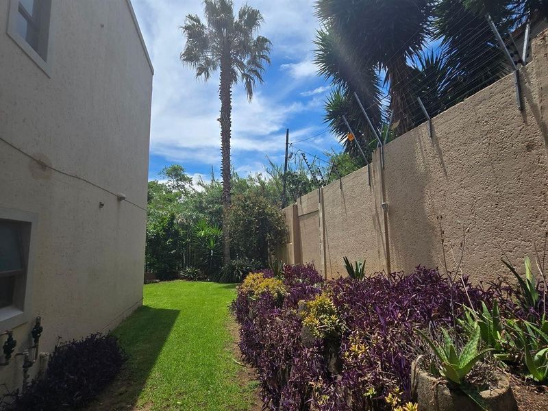 A side garden area featuring a lawn, landscaped garden beds, and a perimeter wall equipped with electric fencing.