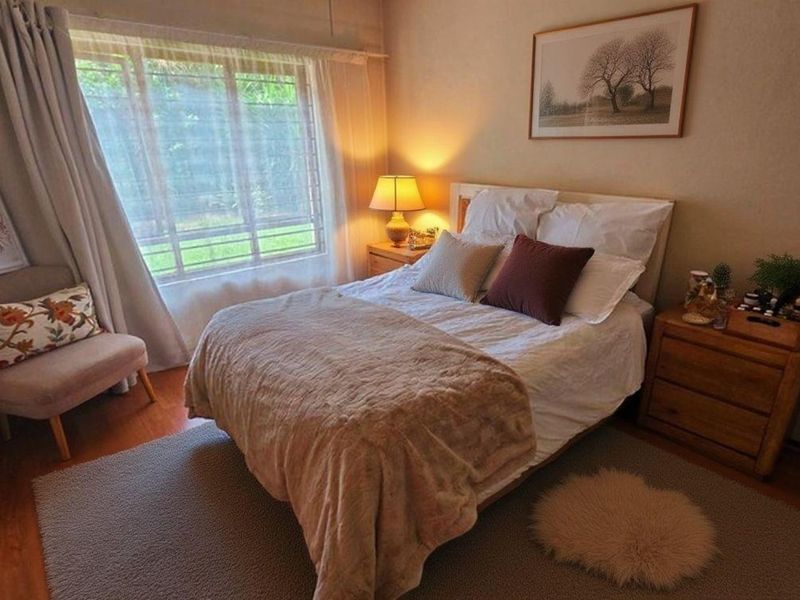 A cozy bedroom featuring warm laminate flooring and a large window that allows for natural light.