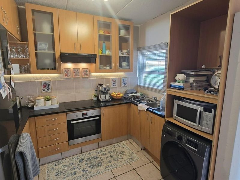 A functional kitchen featuring laminate cabinetry, black granite countertops, built-in oven, electric hob, and integrated laundry appliance space.