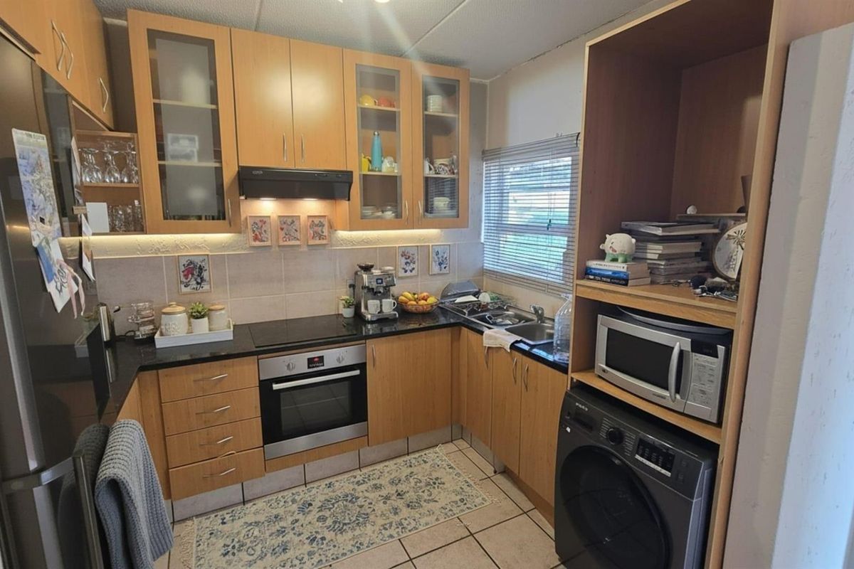 A functional kitchen featuring laminate cabinetry, black granite countertops, built-in oven, electric hob, and integrated laundry appliance space.