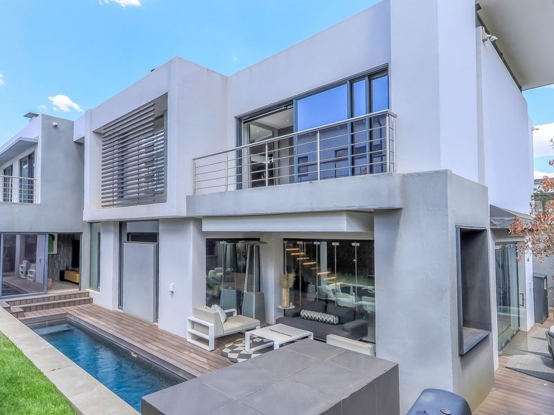 Modern double-storey rear elevation featuring a swimming pool, timber decking, and a spacious upper-level balcony with stainless steel balustrades.