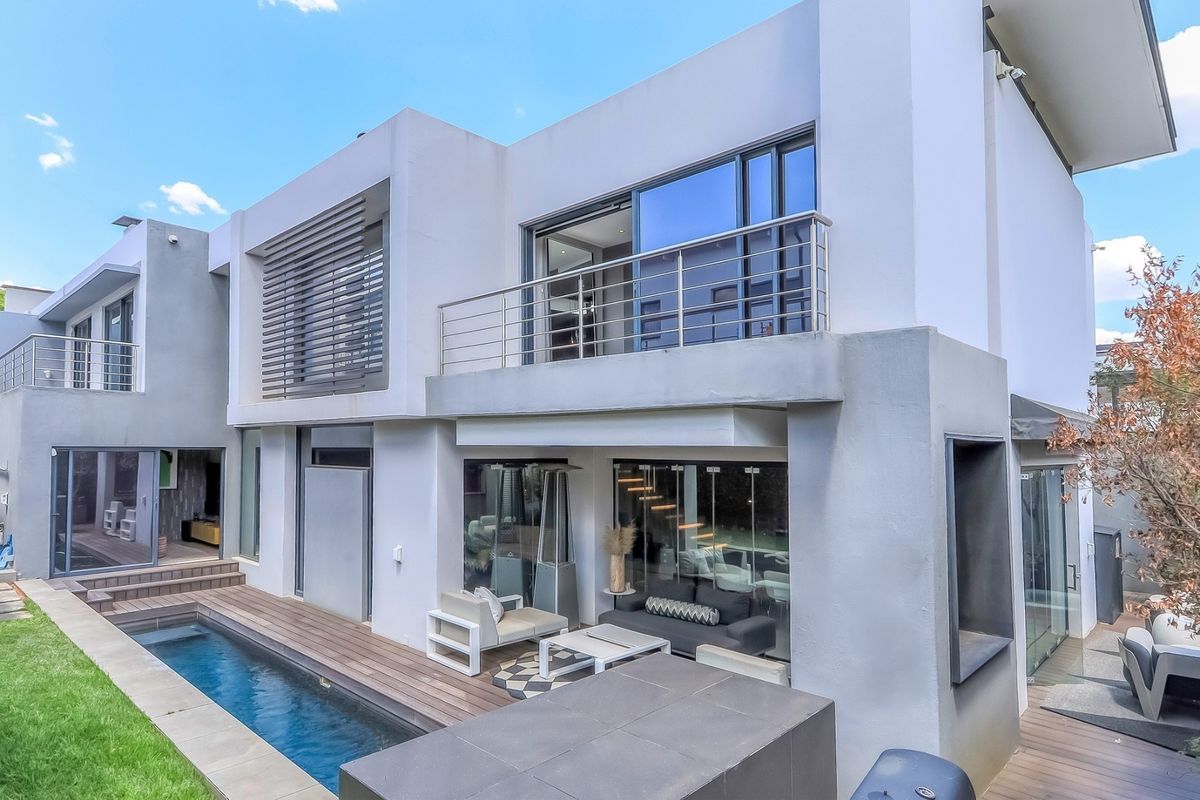 Modern double-storey rear elevation featuring a swimming pool, timber decking, and a spacious upper-level balcony with stainless steel balustrades.