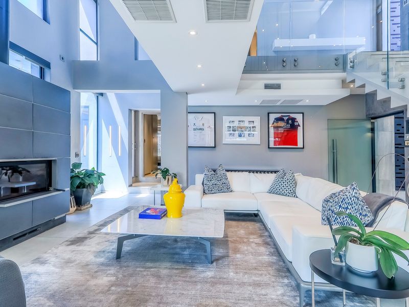Modern double-volume living room featuring a sleek built-in fireplace, glass staircase balustrade, and high-end contemporary finishes with abundant natural light.