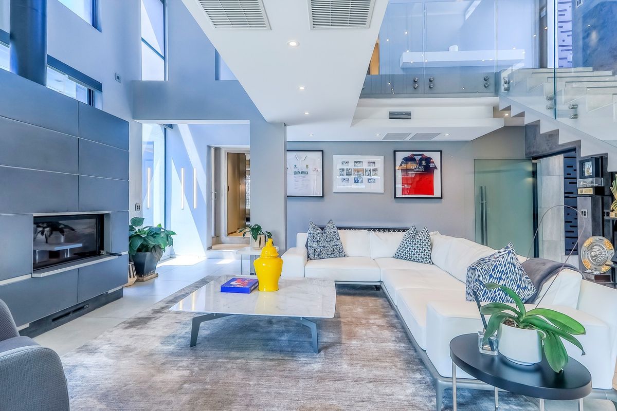 Modern double-volume living room featuring a sleek built-in fireplace, glass staircase balustrade, and high-end contemporary finishes with abundant natural light.
