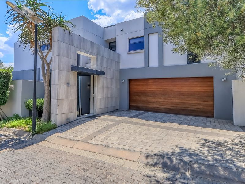 Modern double-storey residential facade featuring stone cladding, a timber garage door, and a paved driveway entrance.