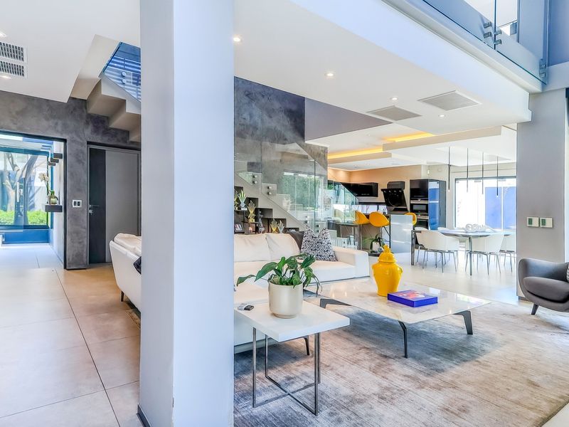 Spacious open-plan living area featuring a modern glass staircase, sleek tiled flooring, and integrated lighting, seamlessly connecting the lounge and kitchen spaces.