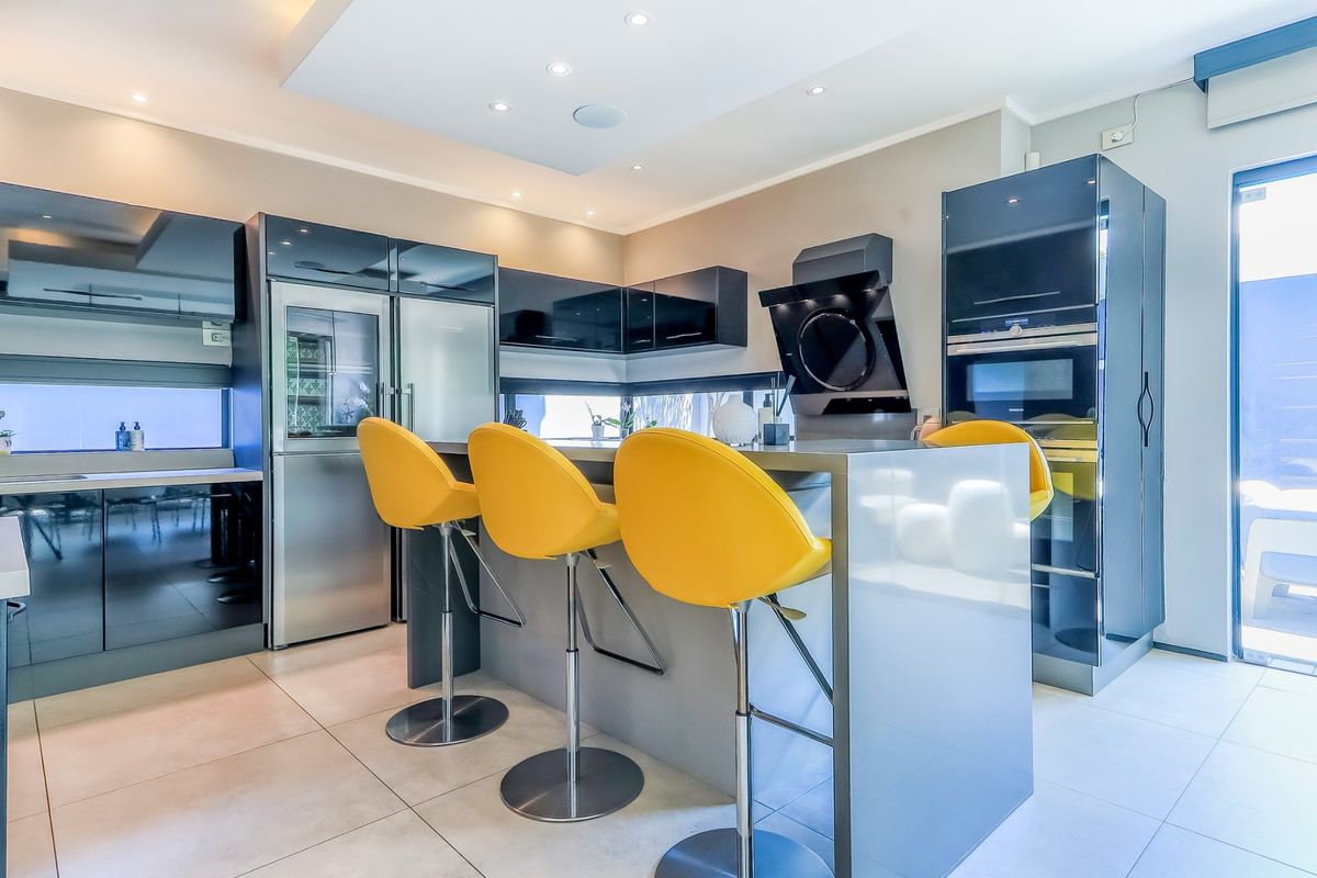 Modern kitchen featuring high-gloss cabinetry, a central island with breakfast bar, integrated appliances, and recessed ceiling lighting.