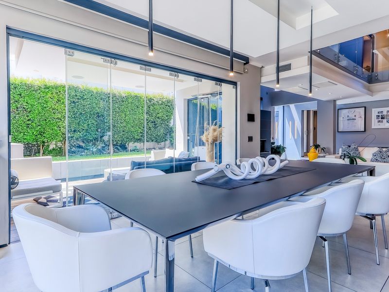 Modern open-plan dining area featuring sleek tiled floors, contemporary pendant lighting, and seamless glass stacking doors opening to a landscaped garden.