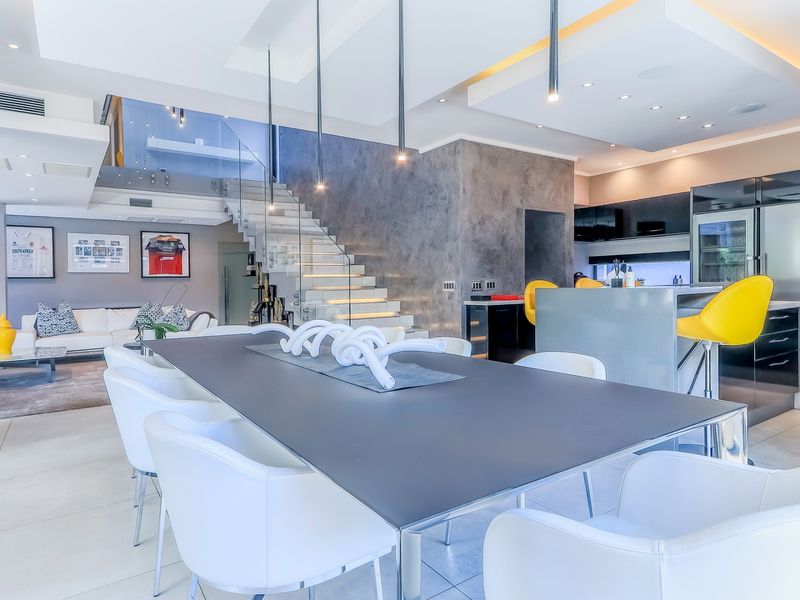 Modern open-plan living and dining area featuring a striking floating staircase with glass balustrade, sleek kitchen cabinetry, and high-end integrated appliances.