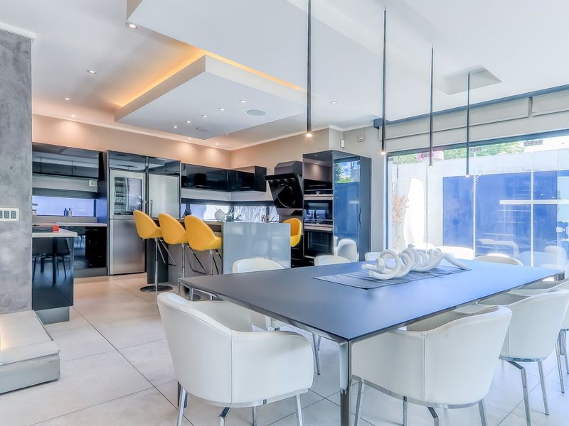 Modern open-plan kitchen and dining area featuring sleek cabinetry, integrated appliances, recessed ceiling lighting, and large sliding glass doors leading to the outdoors.