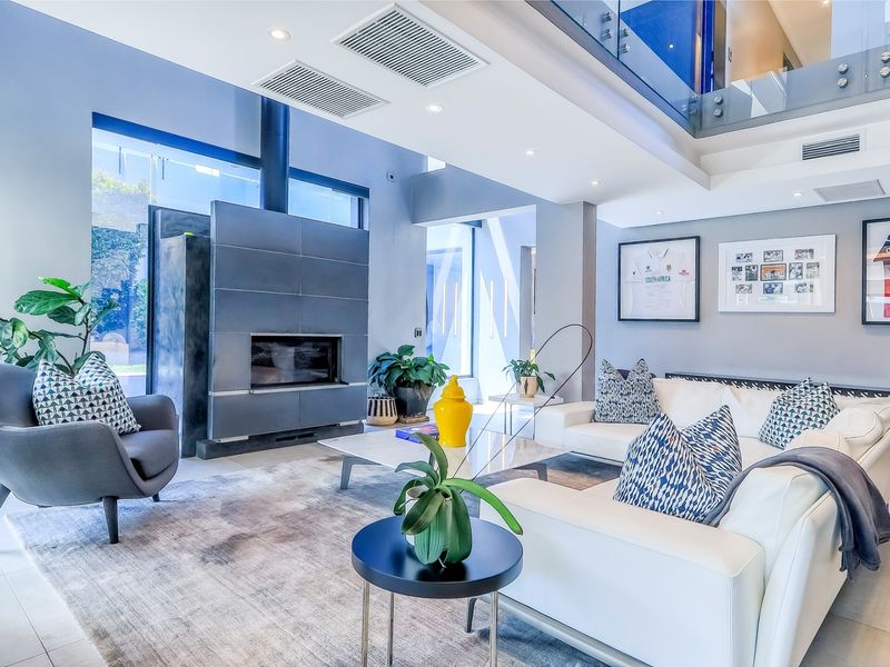 Spacious modern living room featuring a prominent built-in fireplace, high ceilings with recessed lighting, ducted air conditioning, and a sleek glass mezzanine balustrade.