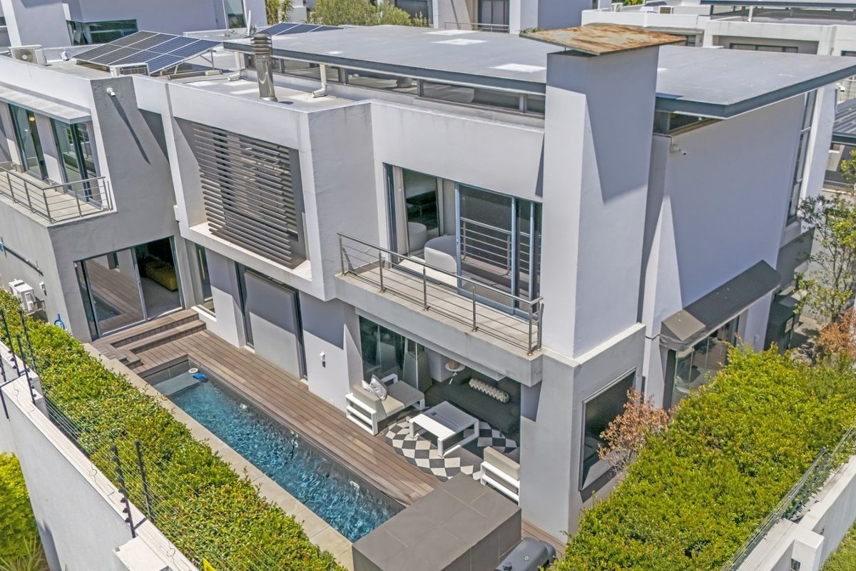 Aerial view of a modern multi-story home featuring a swimming pool, wooden deck, balcony, and solar panels on the roof.