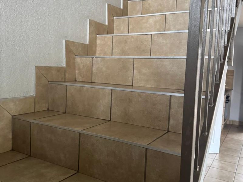 A staircase featuring tiled steps with metal nosing and a sturdy metal handrail, providing a functional transition between levels in the apartment.