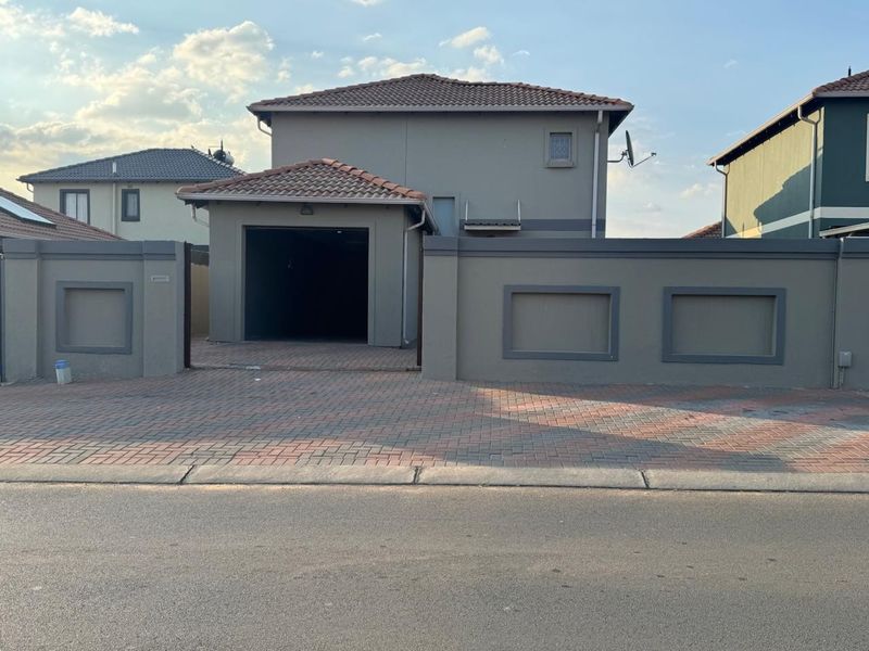 Front elevation of a two-story apartment featuring a paved driveway, secure boundary wall, and an integrated garage.