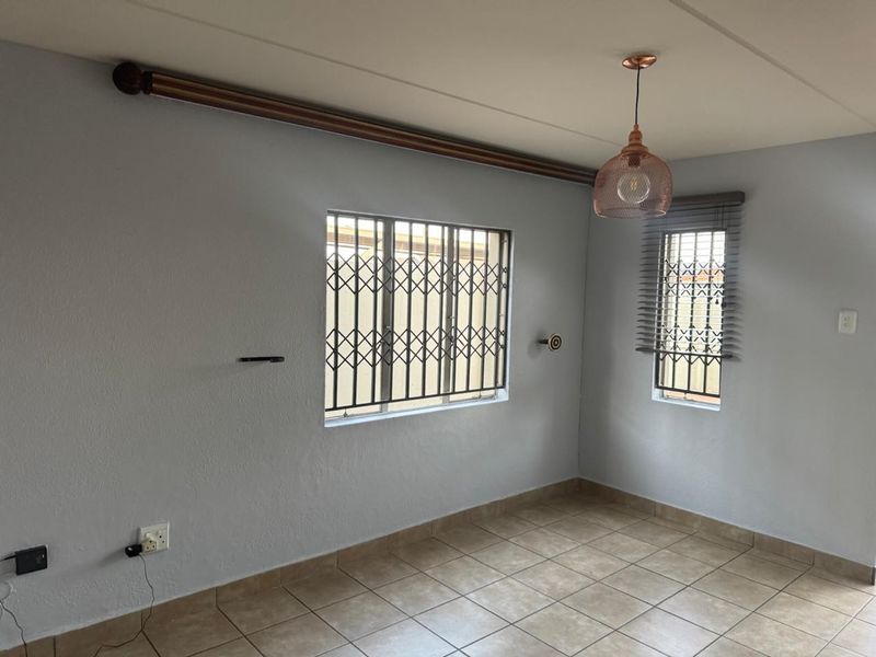 An empty living area featuring tiled flooring, security bars on windows, and a modern pendant light fixture.