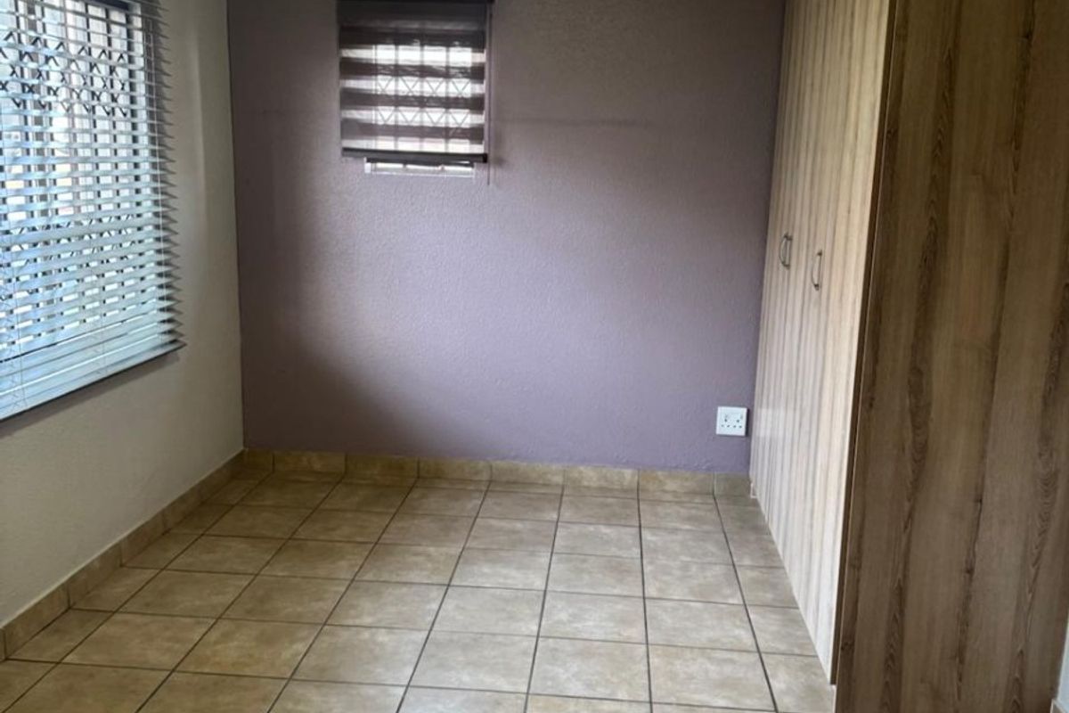 A clean, empty bedroom featuring tiled flooring, built-in wooden cupboards, and dual window treatments, providing a neutral space ready for personalization.