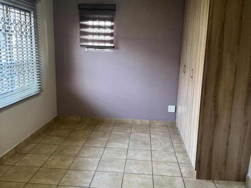 A clean, empty bedroom featuring tiled flooring, built-in wooden cupboards, and dual window treatments, providing a neutral space ready for personalization.