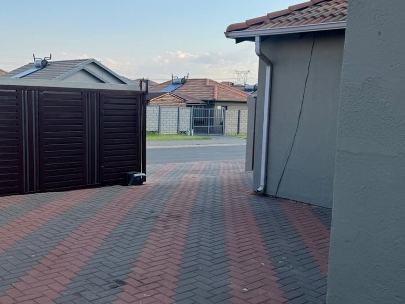 Exterior view of the property entrance featuring a paved driveway, metal gate, and tiled roof structure.