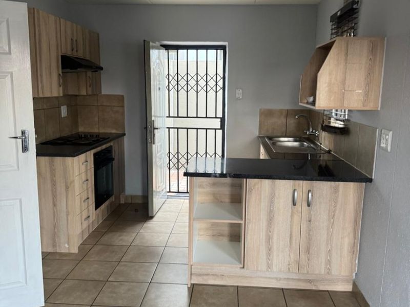 A functional kitchen featuring light wood-finish cabinetry, dark countertops, built-in oven and hob, and tiled flooring with direct access to an exterior security gate.