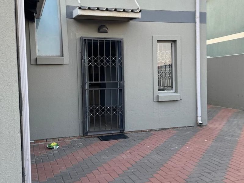 Rear exterior view of the apartment featuring a paved courtyard, security gate, and functional drainage downpipes.