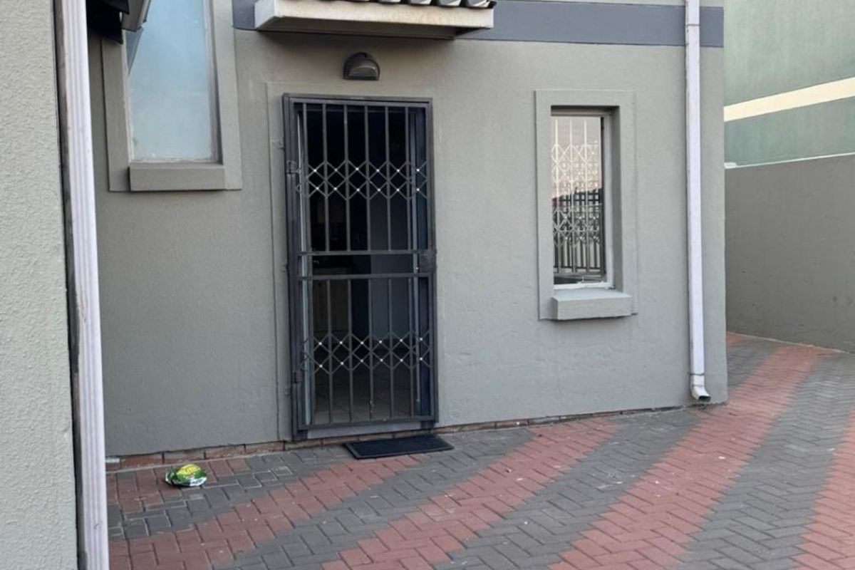 Rear exterior view of the apartment featuring a paved courtyard, security gate, and functional drainage downpipes.