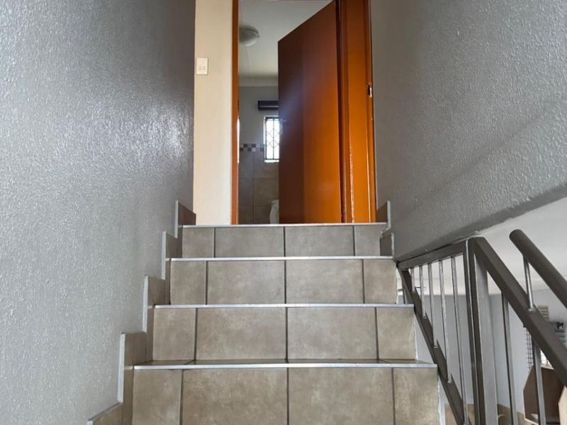 A staircase with tiled steps and a metal handrail leading to an upper level landing with access to an adjacent room.