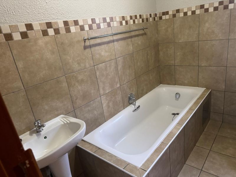 A functional bathroom featuring a built-in bathtub, pedestal basin, and neutral tiled finishes with a decorative border.