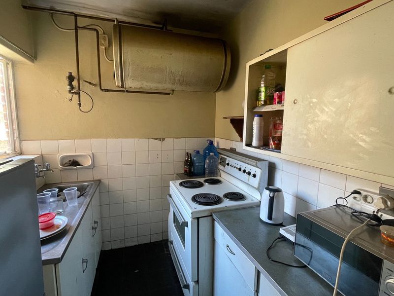 A compact kitchen featuring a built-in electric stove, stainless steel sink, and wall-mounted geyser, requiring significant renovation and cosmetic updates.