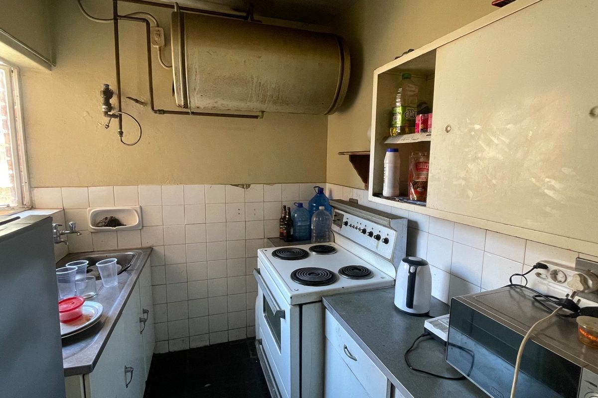 A compact kitchen featuring a built-in electric stove, stainless steel sink, and wall-mounted geyser, requiring significant renovation and cosmetic updates.