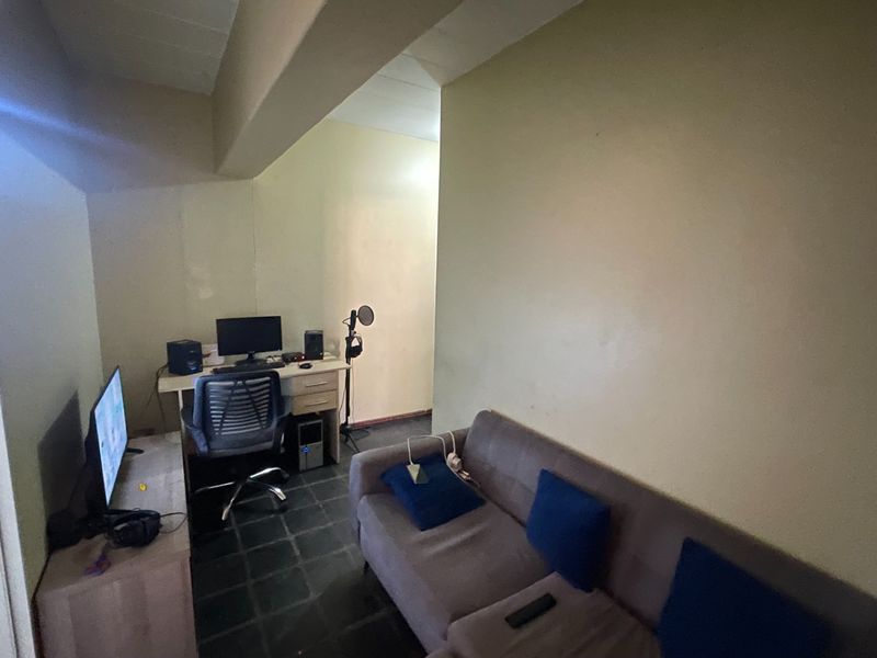 A compact living area featuring tiled flooring and a structural ceiling beam, currently utilized as a multi-purpose workspace and lounge area.