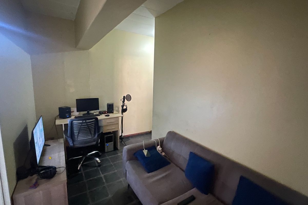 A compact living area featuring tiled flooring and a structural ceiling beam, currently utilized as a multi-purpose workspace and lounge area.