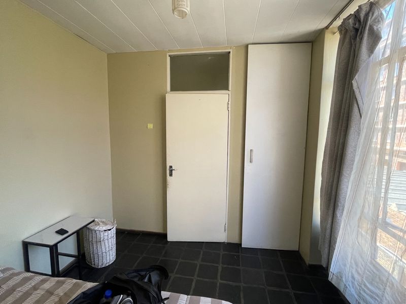 A bedroom featuring dark tiled flooring, a built-in cupboard, and a transom window above the door, offering a functional space ready for modernization.