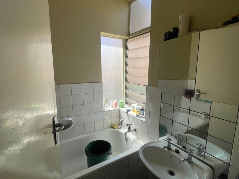 A compact bathroom featuring a bathtub, pedestal basin, and tiled splashbacks. The space includes a medicine cabinet and a functional louvre window.