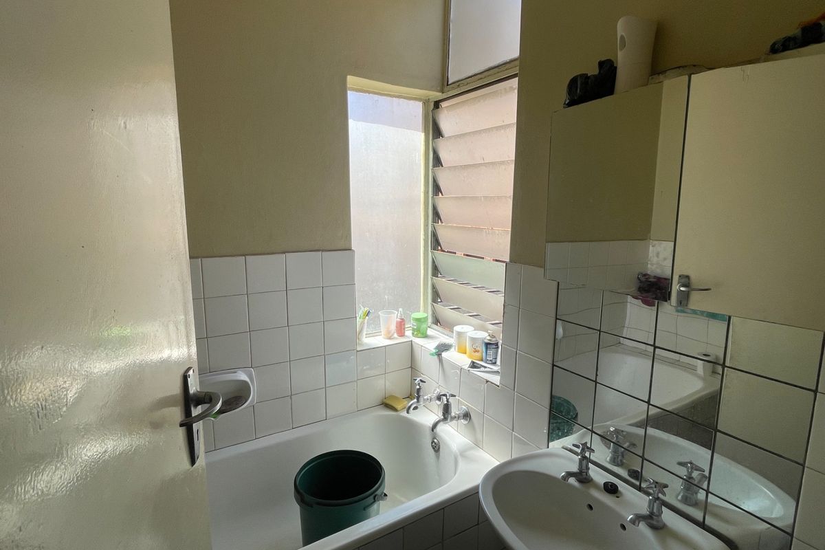 A compact bathroom featuring a bathtub, pedestal basin, and tiled splashbacks. The space includes a medicine cabinet and a functional louvre window.