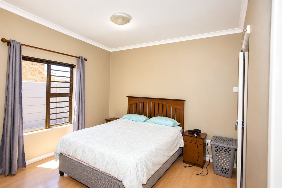 A well-lit bedroom featuring laminate flooring, neutral wall tones, and a built-in cupboard, providing a comfortable and functional living space.
