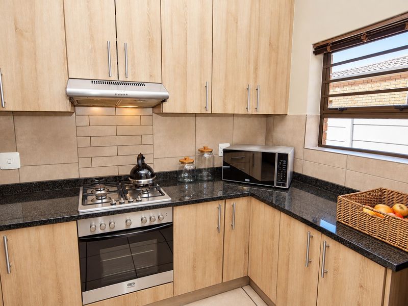 Modern kitchen featuring light wood cabinetry, granite countertops, a gas hob, built-in oven, and a tiled backsplash with a window for natural light.