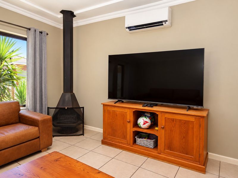 A comfortable living room featuring a freestanding fireplace, split-system air conditioning, and neutral tiled flooring with crown molding details.
