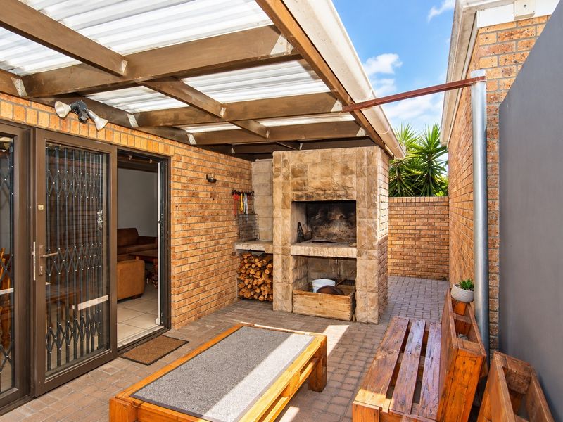 Covered outdoor patio area featuring a built-in brick braai, timber pergola structure, and paved flooring, providing a functional space for outdoor entertaining.