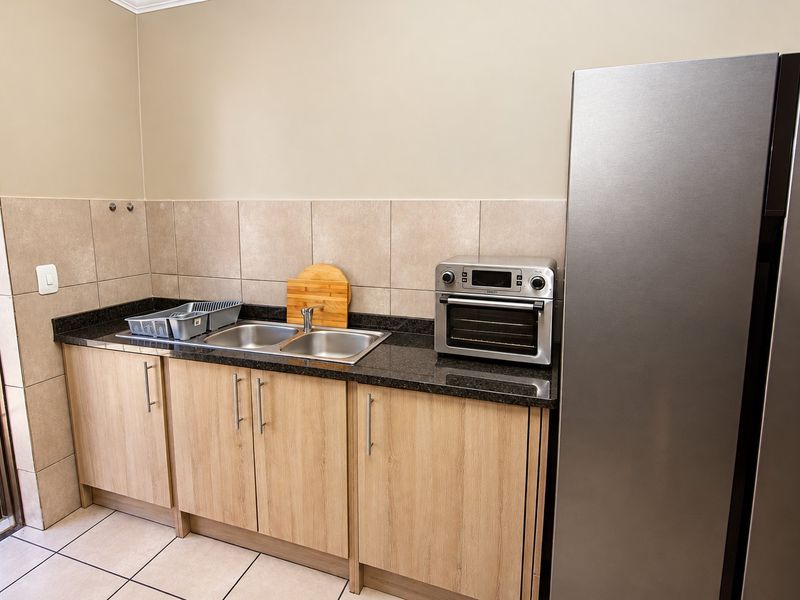 A functional scullery area featuring laminate cabinetry, granite countertops, a double bowl stainless steel sink, and neutral ceramic wall and floor tiling.