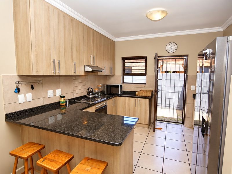 A functional kitchen featuring light wood cabinetry, dark granite countertops, a gas hob with extractor, and direct access to an outdoor area.