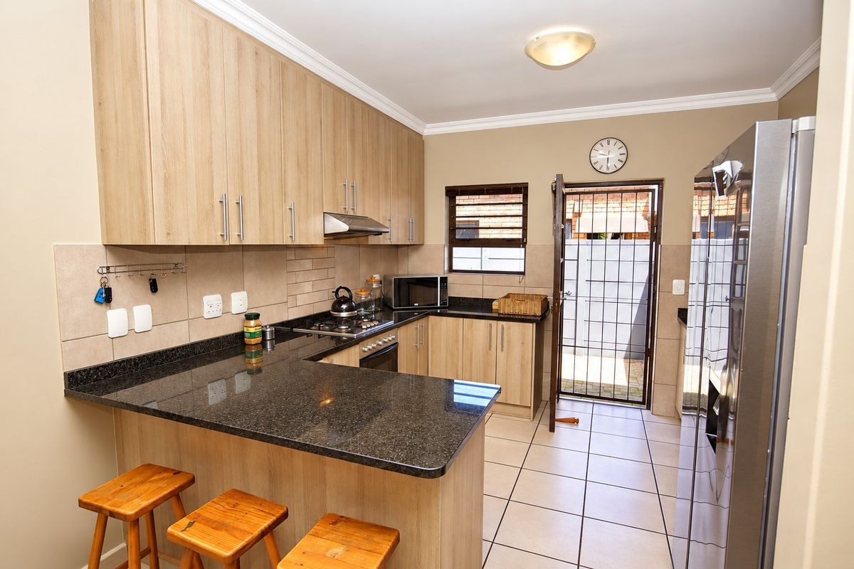 A functional kitchen featuring light wood cabinetry, dark granite countertops, a gas hob with extractor, and direct access to an outdoor area.
