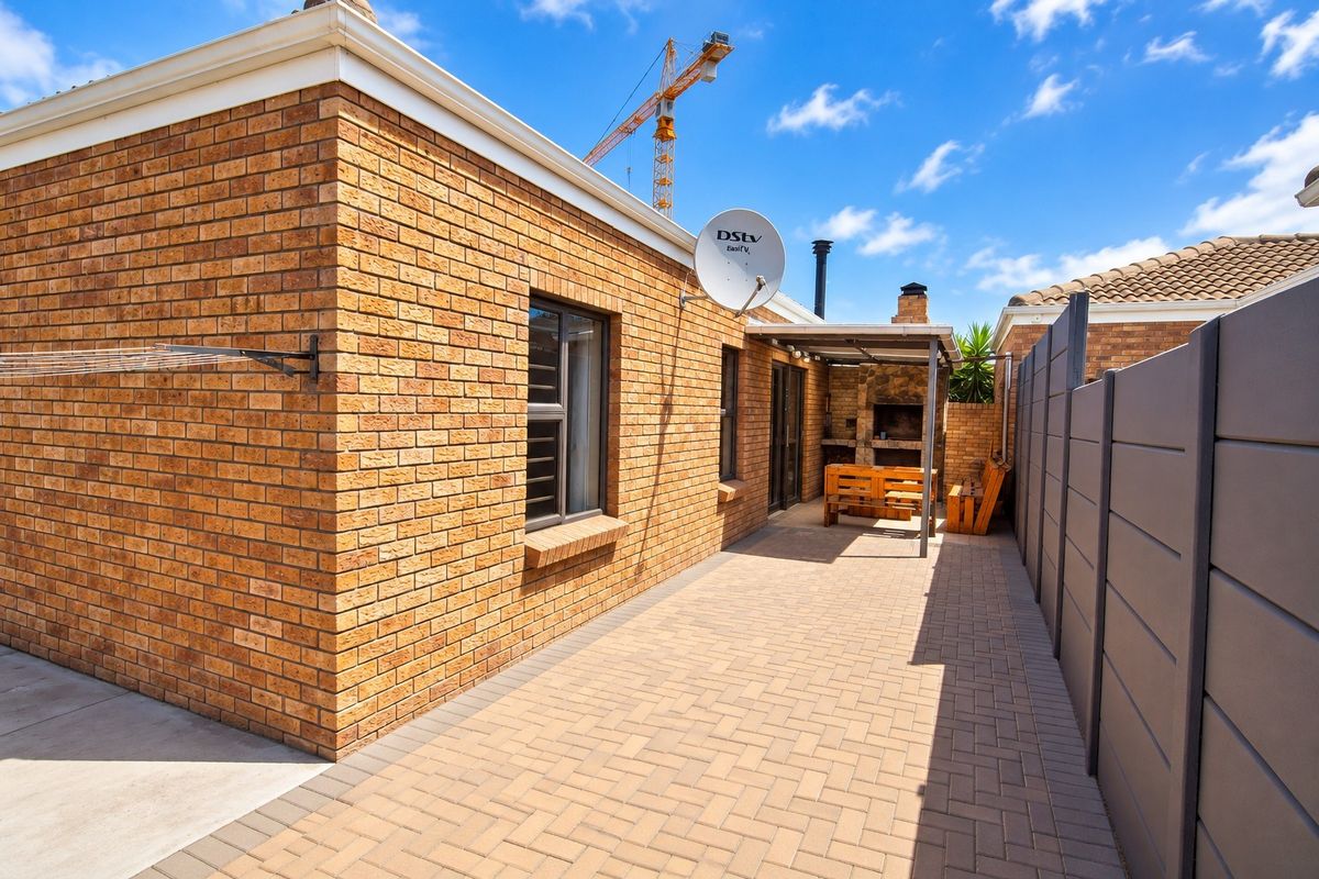 A well-maintained rear exterior featuring a paved patio area, a built-in braai, and face brick walling, providing a functional outdoor entertainment space.
