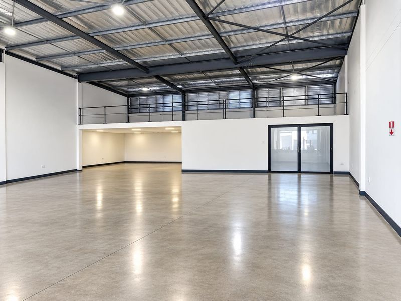 Spacious industrial open-plan warehouse area featuring polished concrete floors, high exposed steel ceilings, and a functional mezzanine level with modern glass entry.