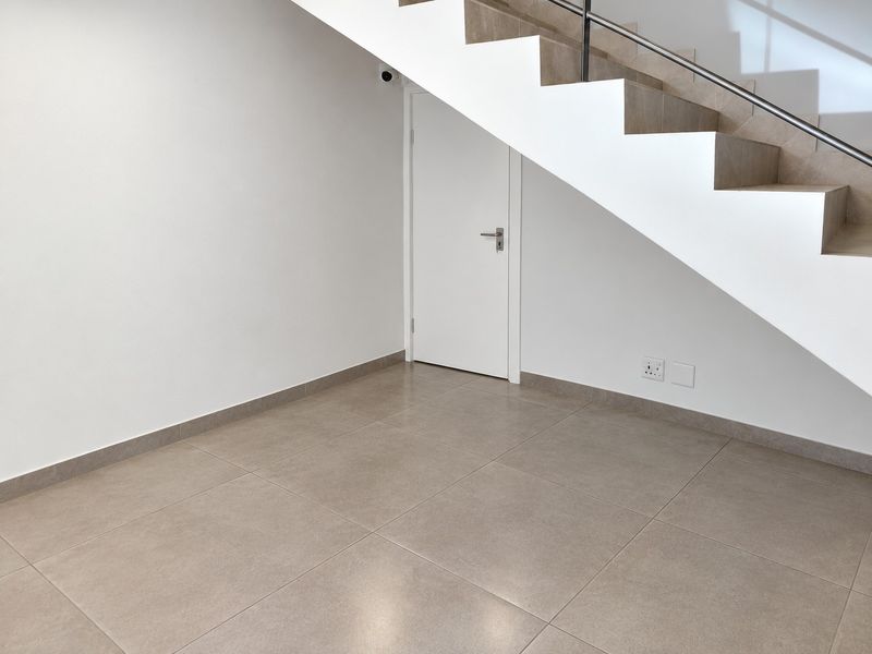 A clean, modern hallway area featuring neutral floor tiles, a staircase with a metal handrail, and integrated security camera.
