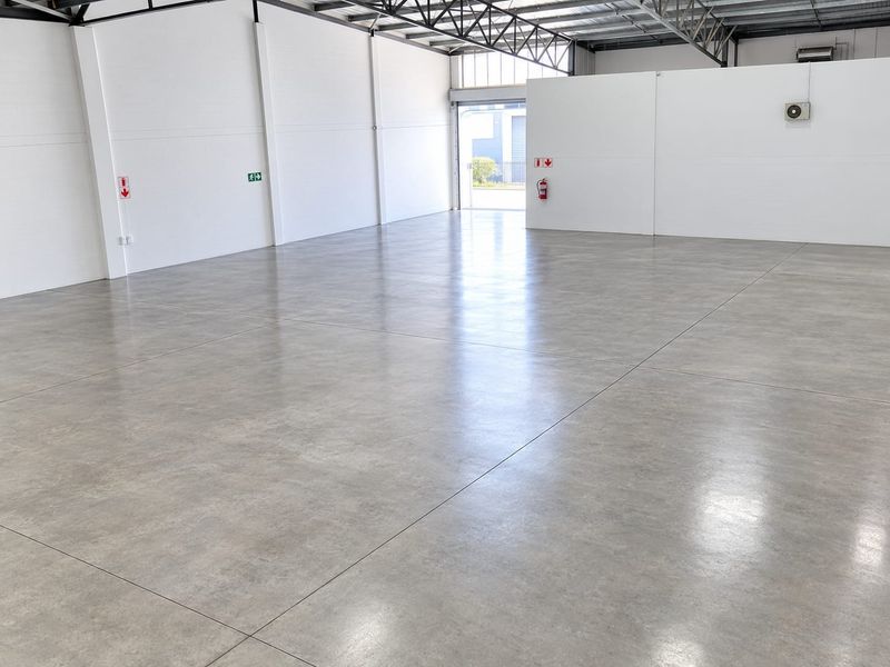 Spacious industrial warehouse unit featuring polished concrete flooring, exposed steel roof trusses, and a large roller door for easy access.
