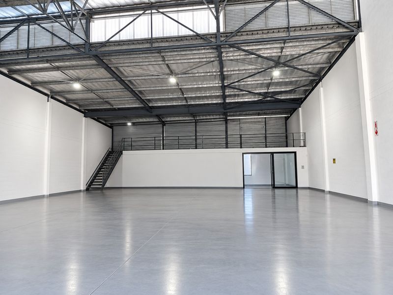 Spacious industrial warehouse unit featuring high ceilings with exposed steel trusses, polished concrete flooring, a mezzanine level, and integrated office space.