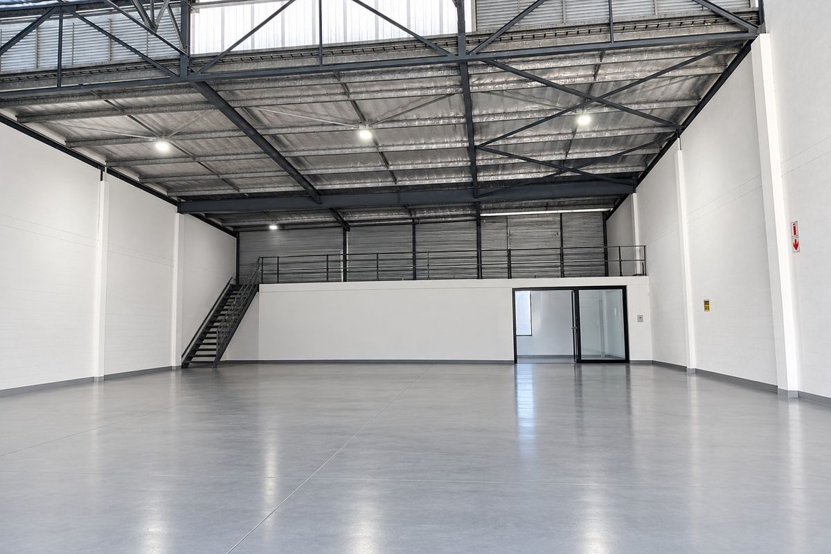 Spacious industrial warehouse unit featuring high ceilings with exposed steel trusses, polished concrete flooring, a mezzanine level, and integrated office space.