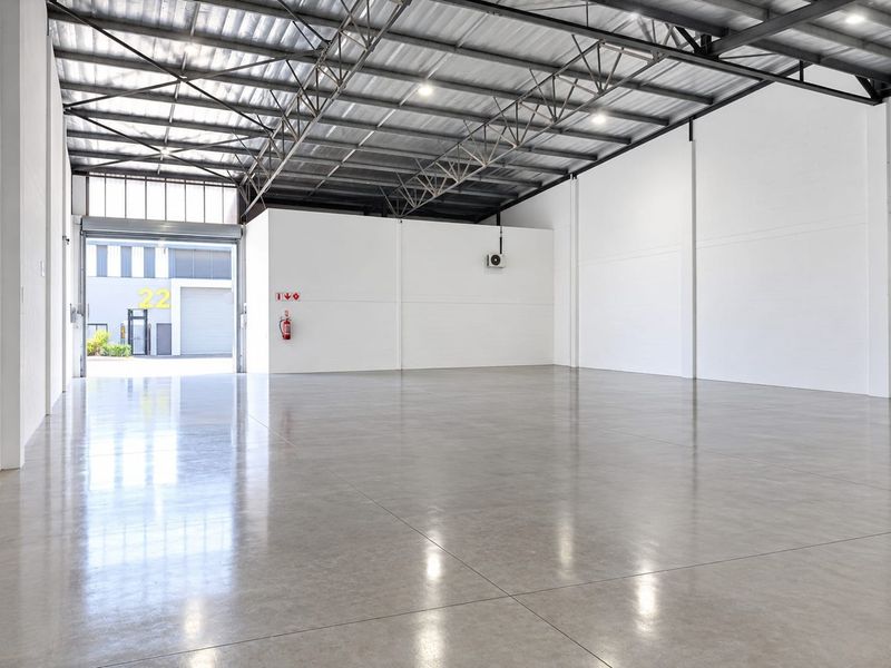 Spacious industrial warehouse unit featuring polished concrete flooring, high exposed steel roof trusses, and a large roller shutter door for easy access.