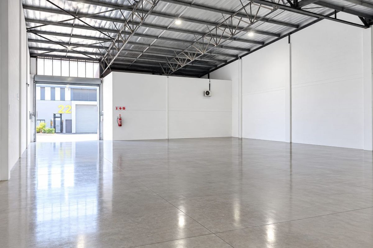 Spacious industrial warehouse unit featuring polished concrete flooring, high exposed steel roof trusses, and a large roller shutter door for easy access.