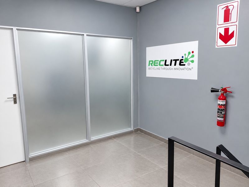 A clean, modern industrial entrance area featuring tiled flooring, a frosted glass partition, and essential fire safety equipment mounted on a grey wall.
